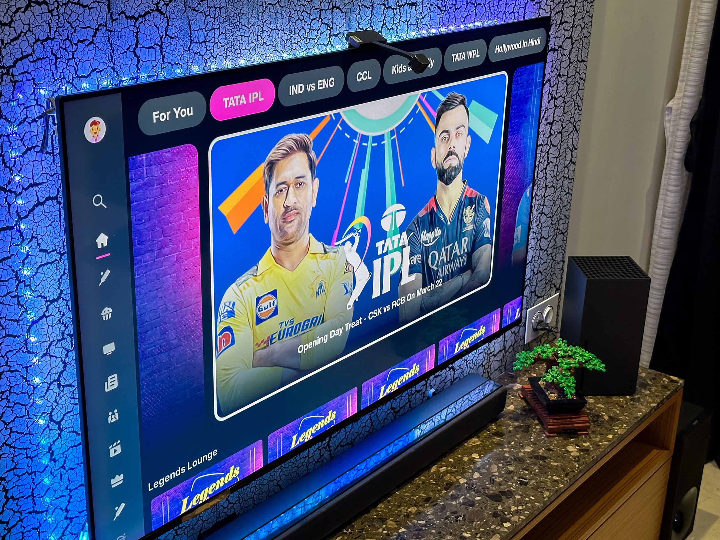 MS Dhoni of Chennai Super Kings and Virat Kohli of Royal Challengers Bangalore in an ad for IPL 2024 on JioCinema on OnePlus Q1 TV fitted with Govee TV LED RGBIC backlight with camera. The TV is next to Lego Bonsai Tree, Xbox Series X, and Sony HT-Z9F soundbar.