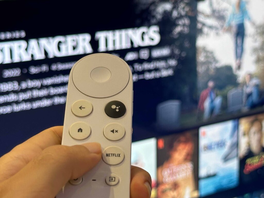 Netflix logo on Chromecast with Google TV remote in front of TV with Stranger Things