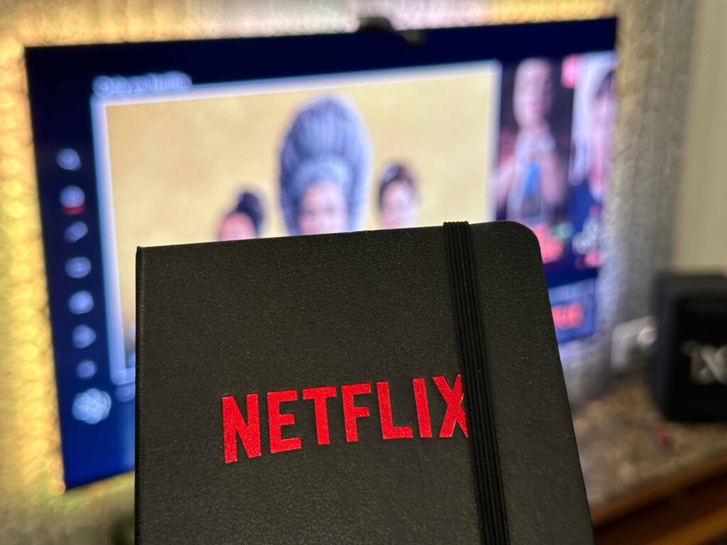 Netflix logo on notepad in front of TV with Queen Charlotte: A Bridgerton Story